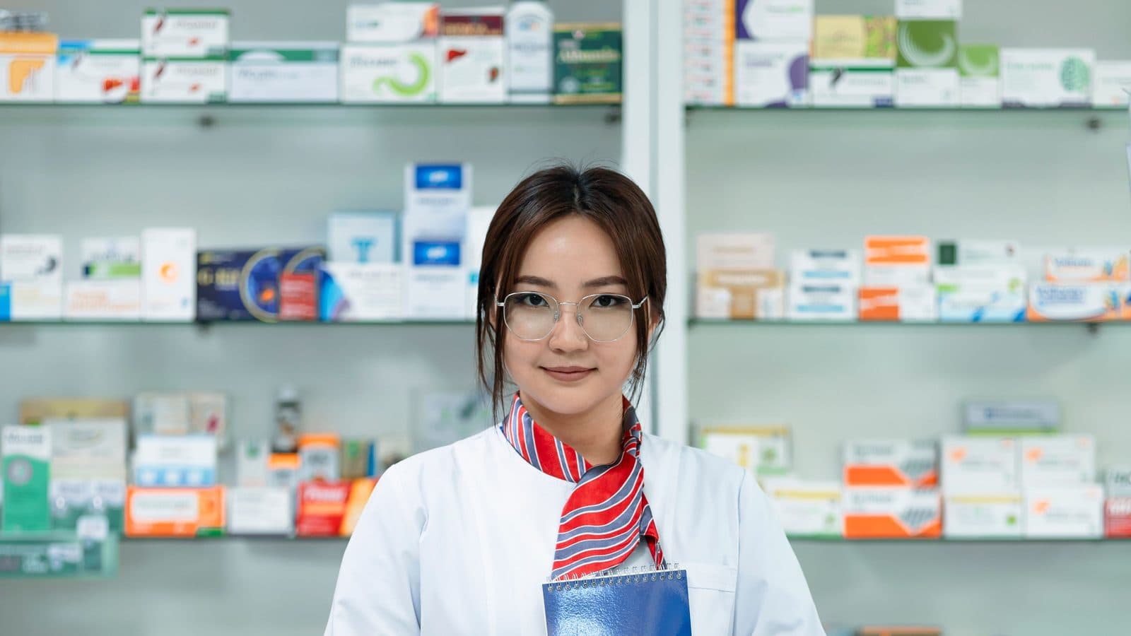 A young pharmacist standing in front of pharmacy shelves